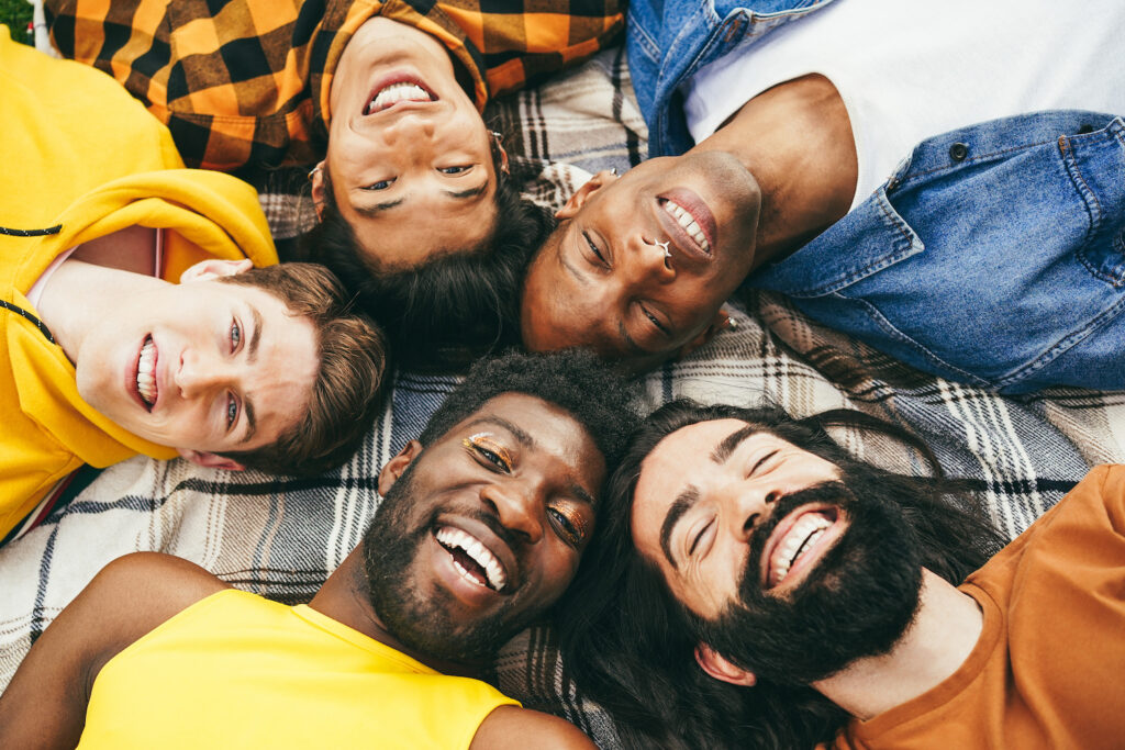 Happy diverse male friends having fun lying together in circle outdoor - Soft focus on blond man